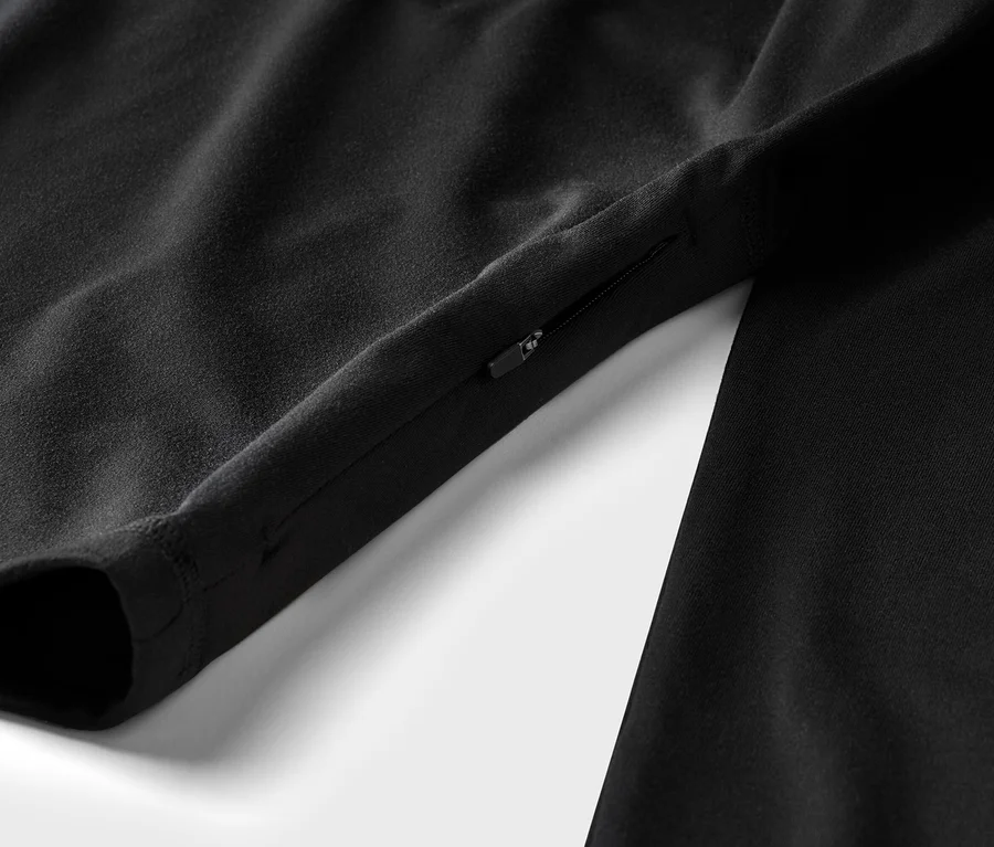 Detail černého oděvu s rukávem a kapsou na zip na bílém pozadí.