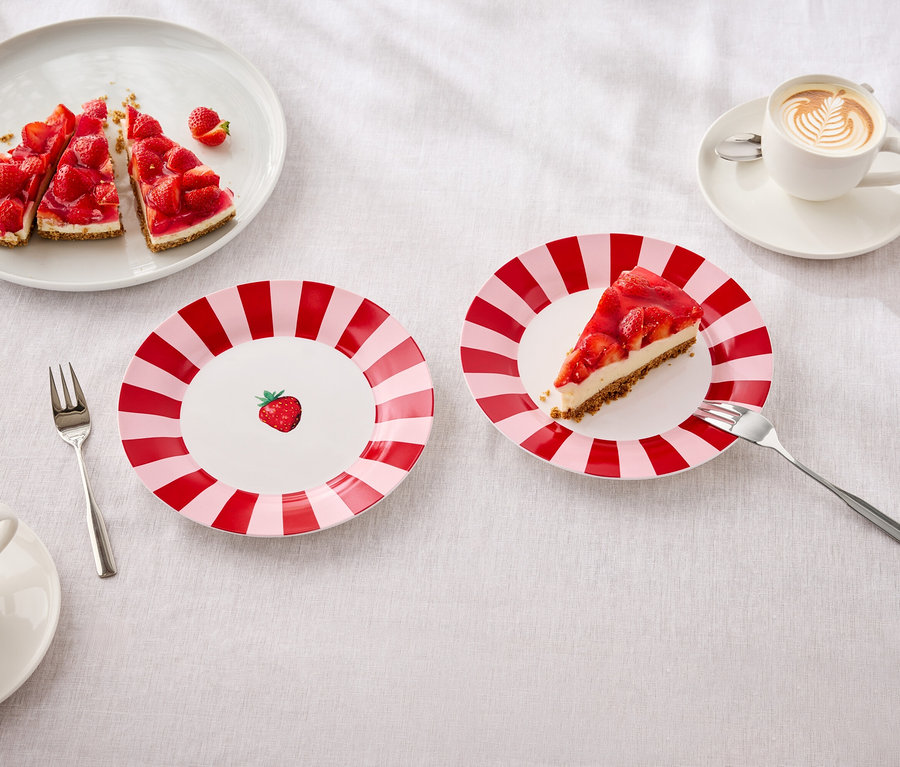 Na stole jsou talíře s jahodovým koláčem, vidličky a šálky s latte art.