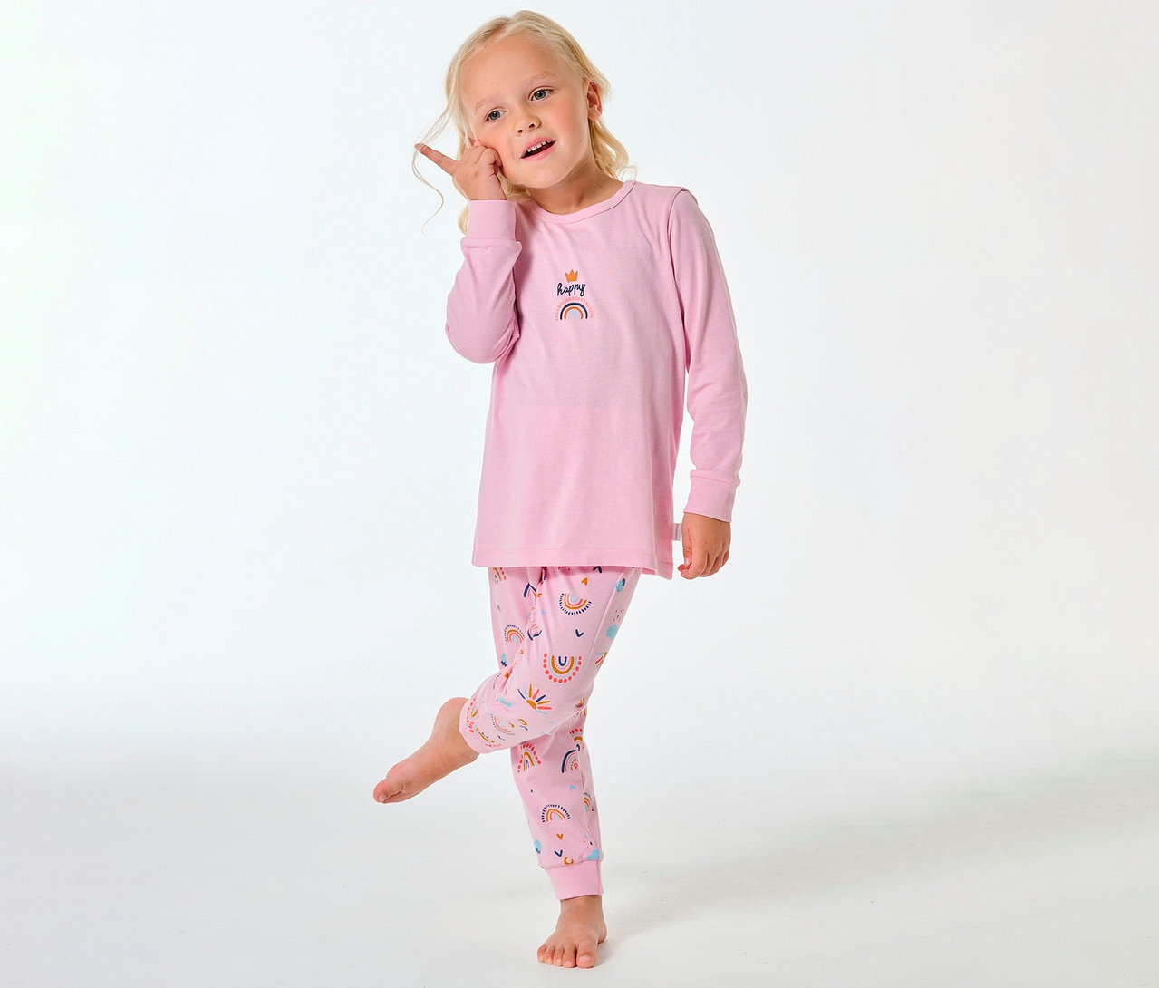 Dívka v dlouhém dětském pyžamu SCHIESSER s duhovým vzorem na kalhotách a horním dílu.