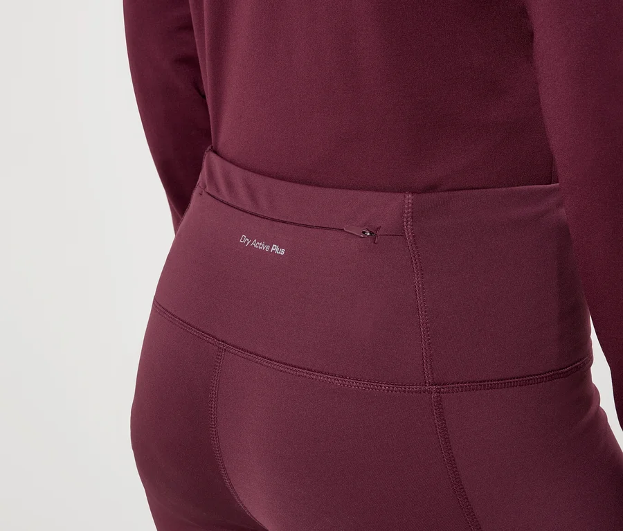 Detailní záběr ženy v bordových legínách a topu s dlouhým rukávem s nápisem „Dry Active Plus“.