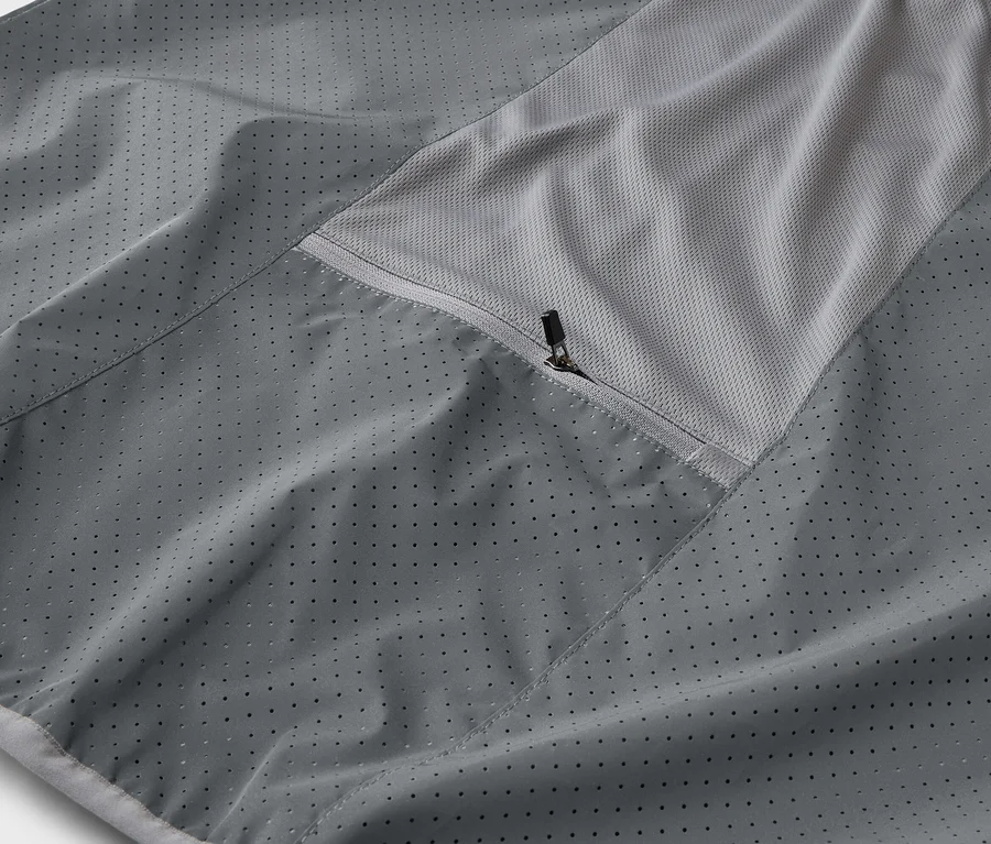 Detail šedé bundy s kapsou na zip a prodyšnou síťovanou vložkou.