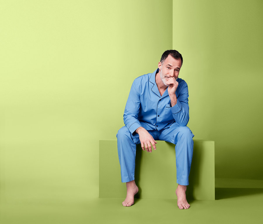 Muž sedí na zeleném bloku a má na sobě modré tkané pyžamo.