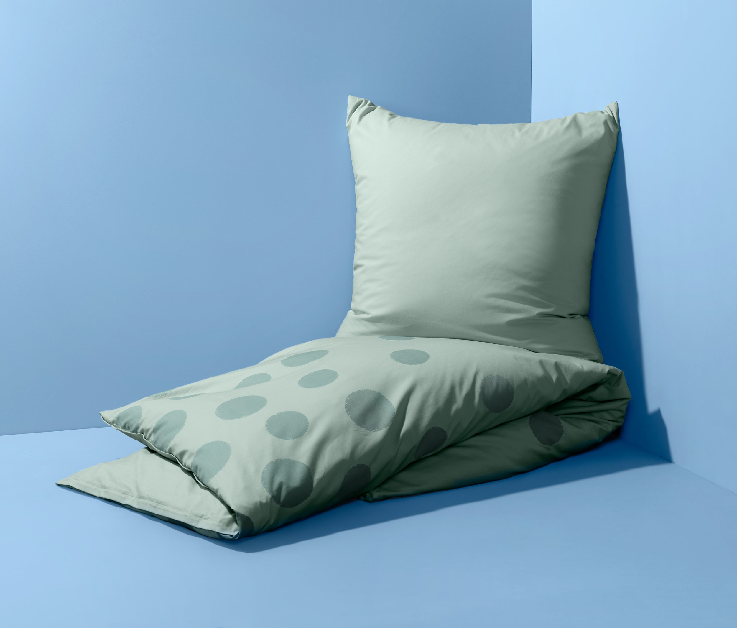 Světle zelené oboustranné perkálové povlečení standardní velikosti s puntíky leží na podlaze u zdi.