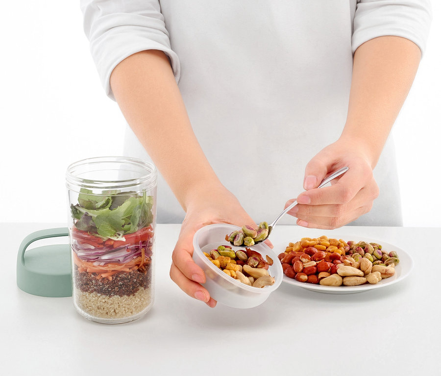 Žena lžící přidává ořechy do cestovní dózy na oběd. 