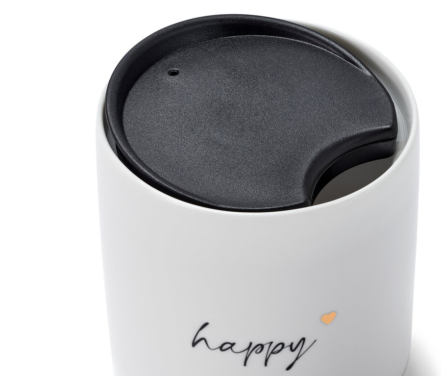 Detail bílého porcelánového hrnku s černým víčkem a nápisem happy.