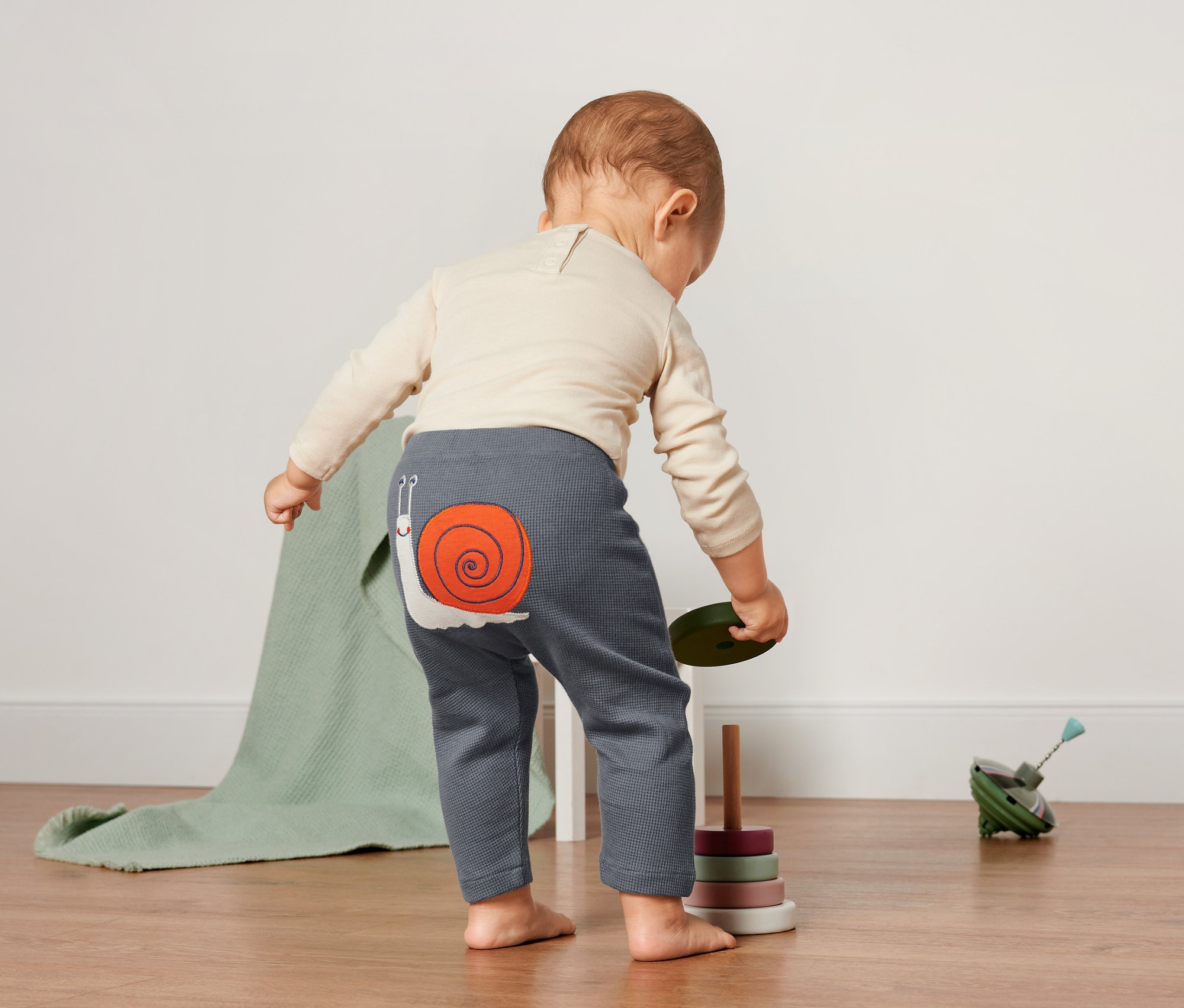 Batole stojí zády a má na sobě vaflové kalhoty s nášivkou šneka.