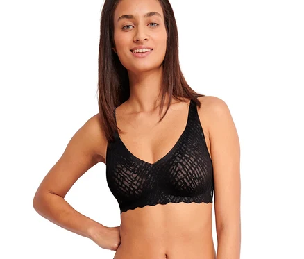 Usmívající se žena v černé měkké podprsence sloggi ZERO Feel Bliss Soft bra a ladících vzorovaných kalhotkách, s rukou na boku.