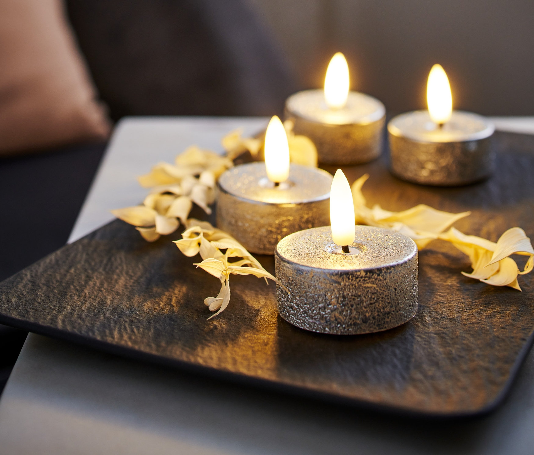 Čtyři stříbrné LED čajové svíčky z pravého vosku na černé podložce, zdobené suchými květy.