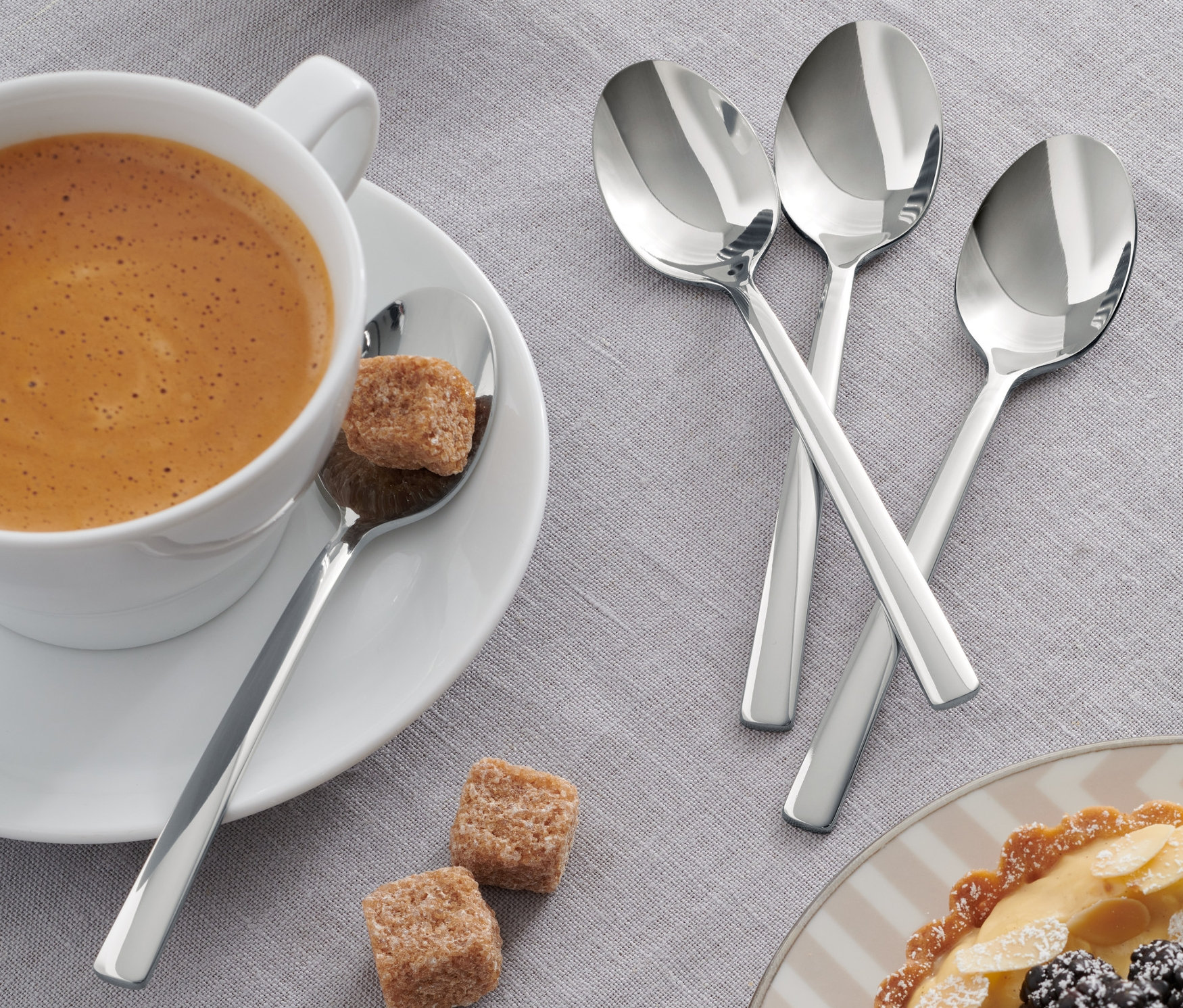 Káva v šálku s kostkami cukru a 4 kávovými lžičkami.