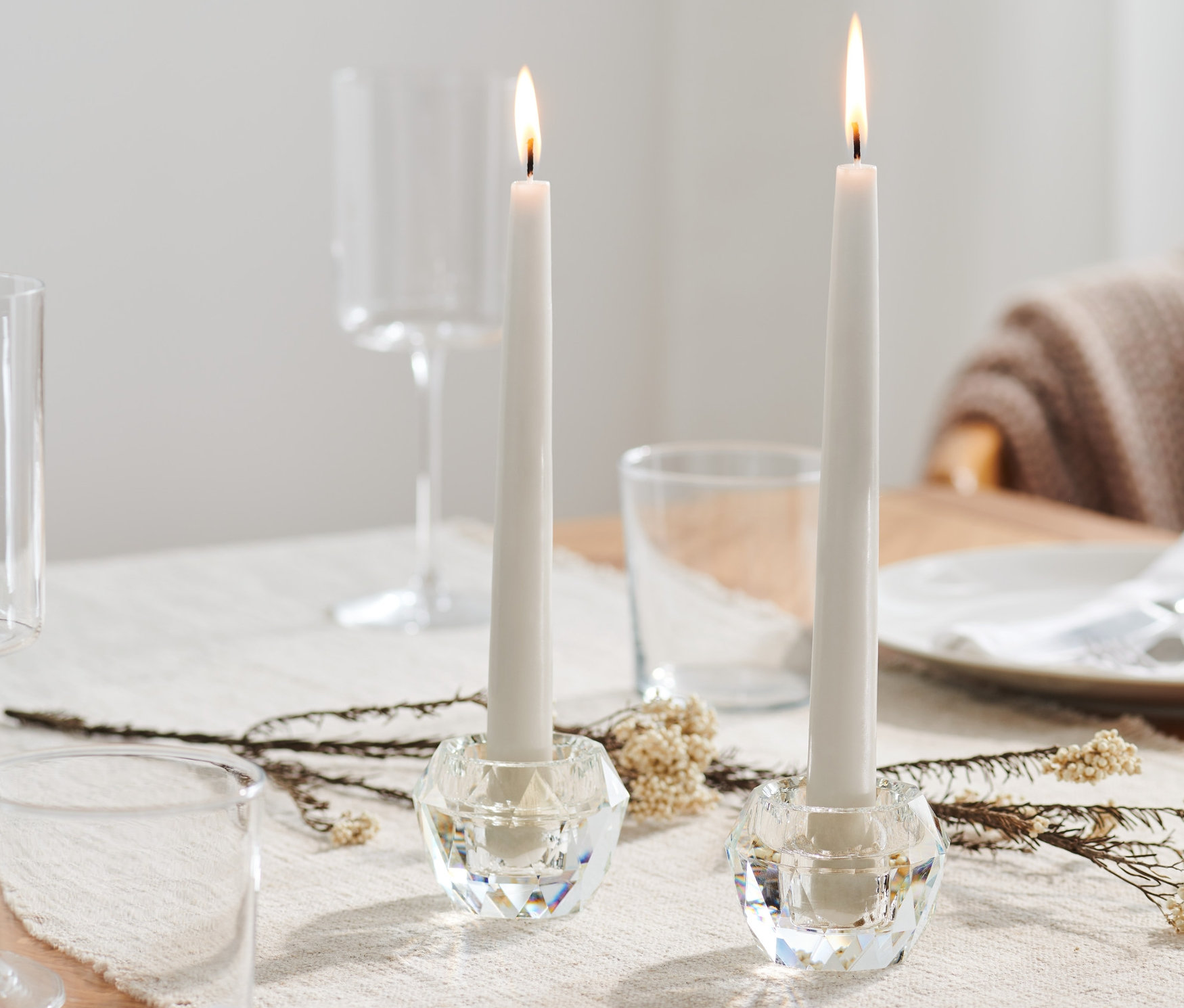 Dva skleněné svícny na stole s hořícími svíčkami.