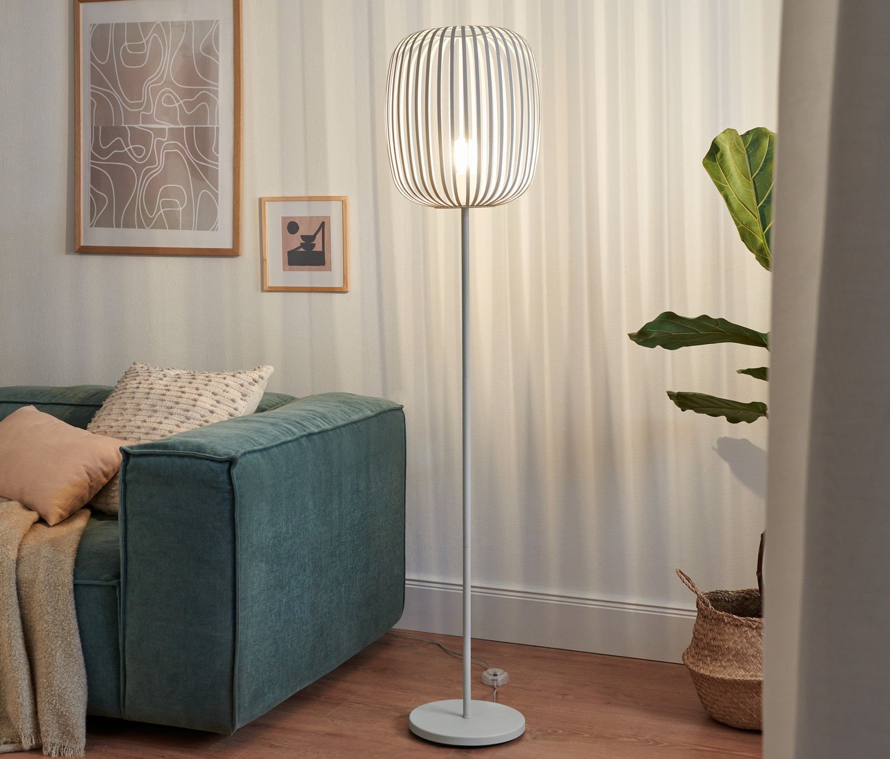 Kovová stojací lampa stojí vedle zelené pohovky v obývacím pokoji.