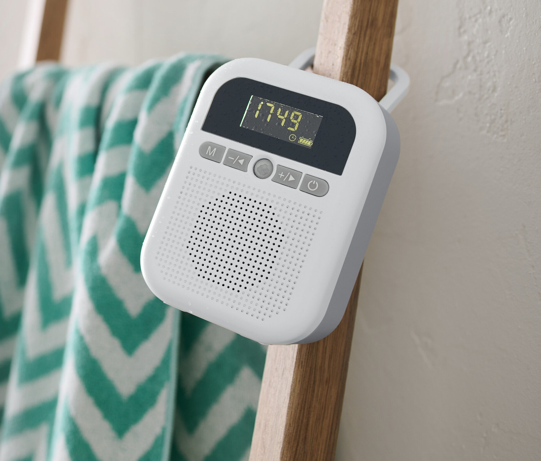 Bílé rádio do koupelny visí na dřevěném žebříku, na kterém je zavěšený ručník.