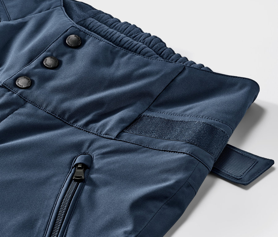 Detail modrých lyžařských kalhot s vysokým pasem. Zapínání na knoflíky, zip a suchý zip.
