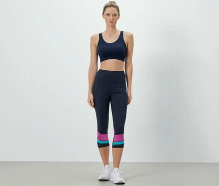 Žena má na sobě sportovní podprsenku a 3/4 sportovní legíny.