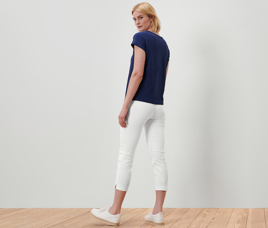 Žena stojí zády k fotoaparátu a má na sobě bílé 7/8 strečové kalhoty a tmavě modré tričko.