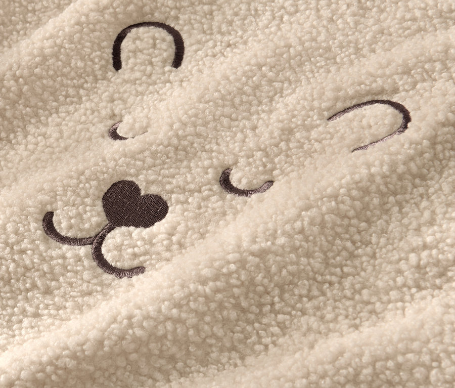 Detail měkoučkého svetru s vyšitým obličejem medvěda.