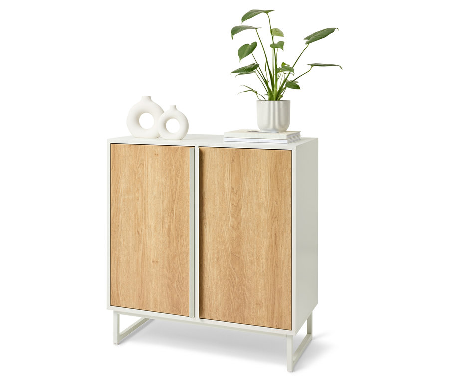 Bílý skříň s dřevěnými dvířky. Na horní části skříně jsou dvě bílé vázy, kniha a květina v bílém květináči.