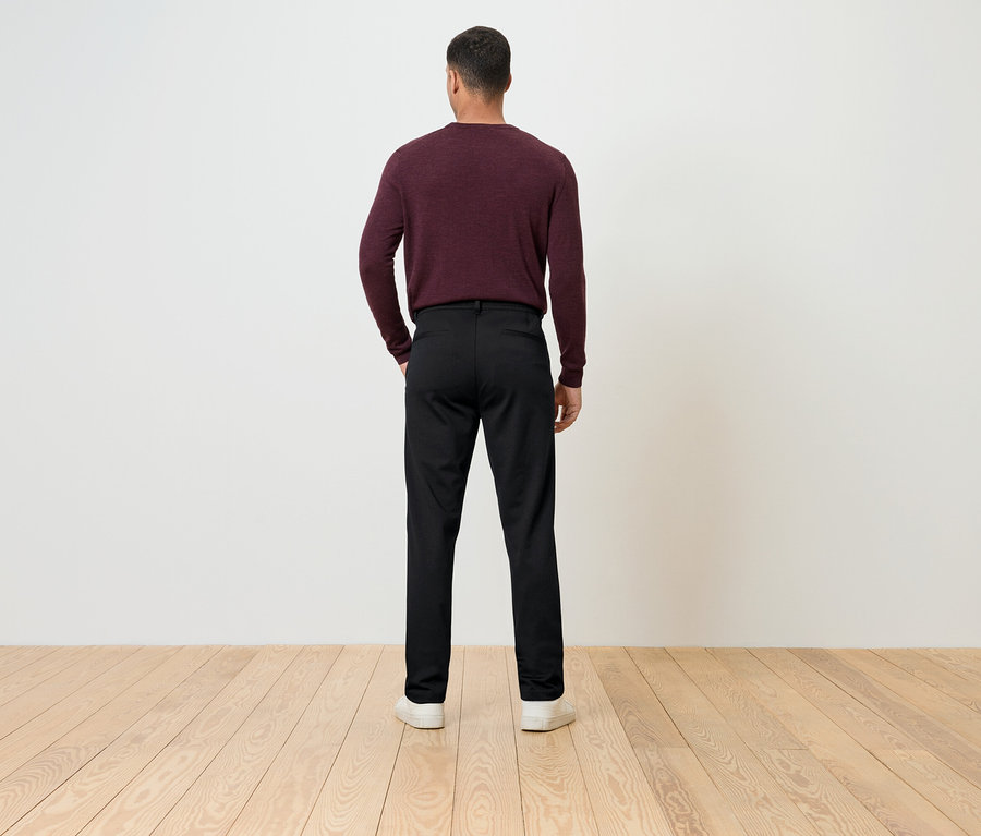 Muž zády k fotoaparátu má na sobě vínový svetr a černé kalhoty.