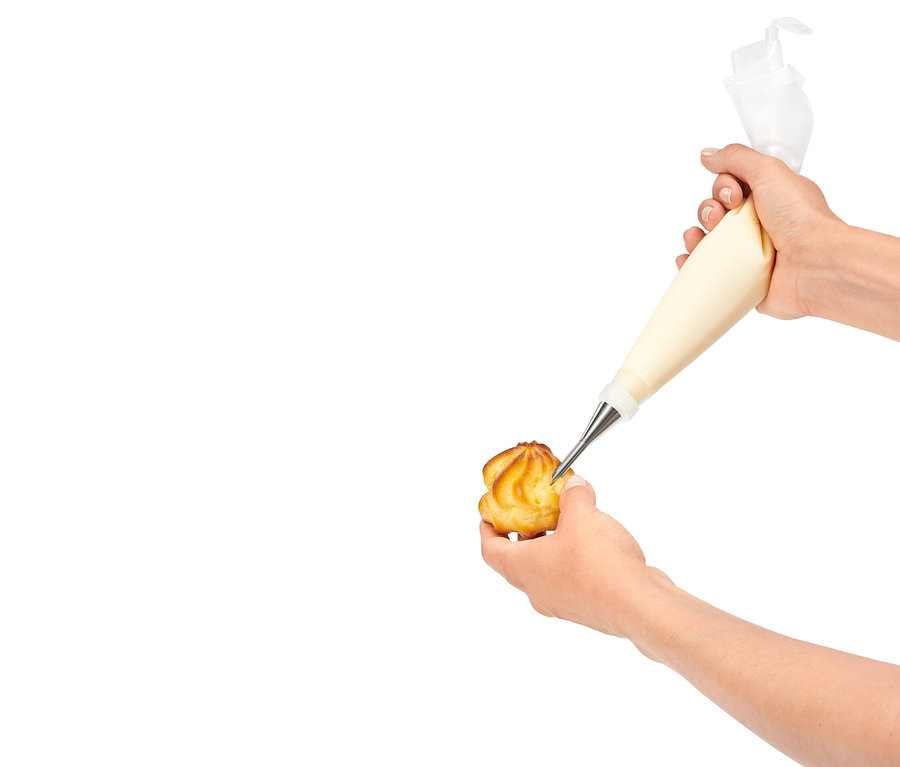 Ruka plní krémem cukrářský výrobek pomocí zdobícího sáčku.