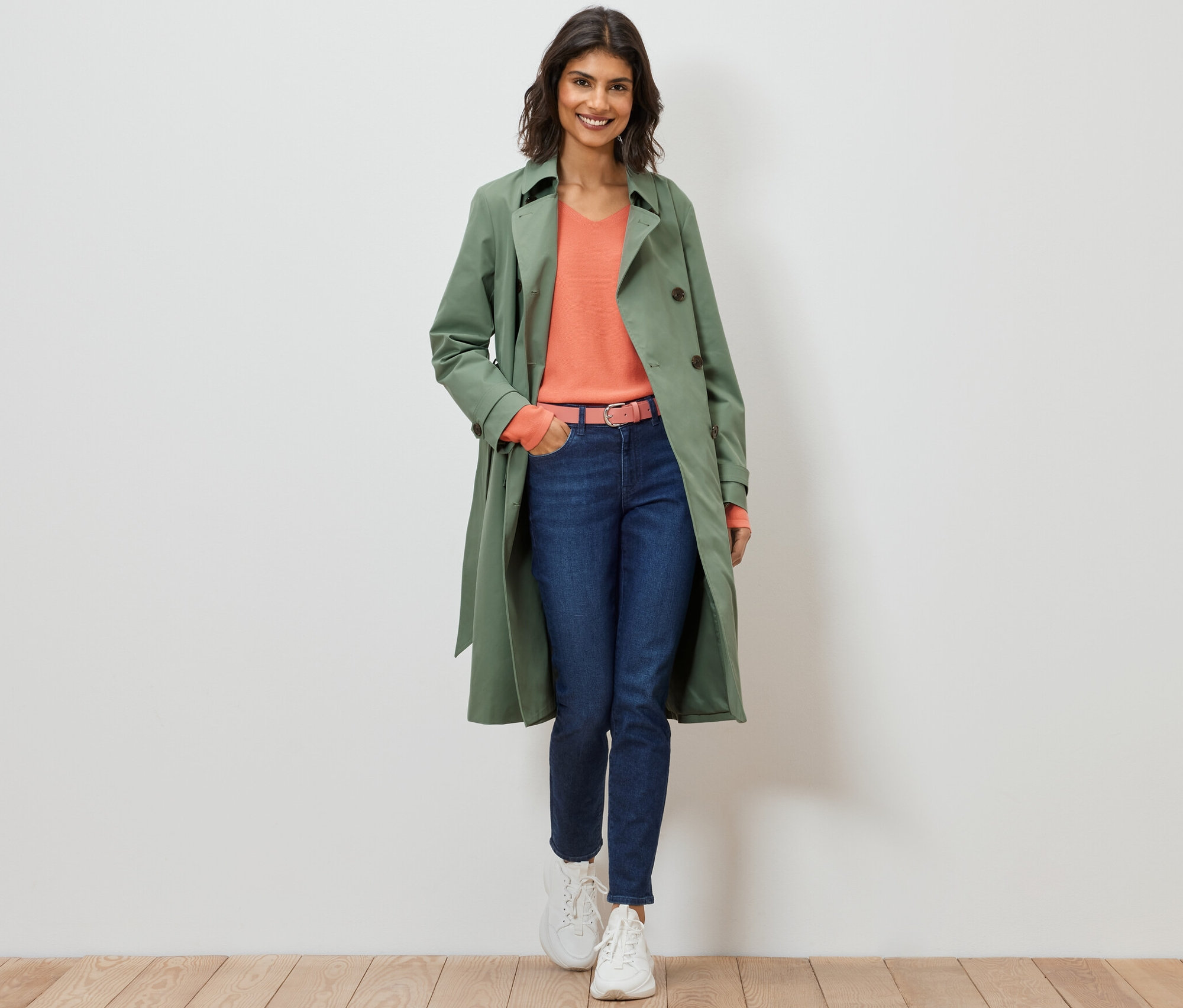 Žena kráčí a má na sobě světle zelený trenčkot.