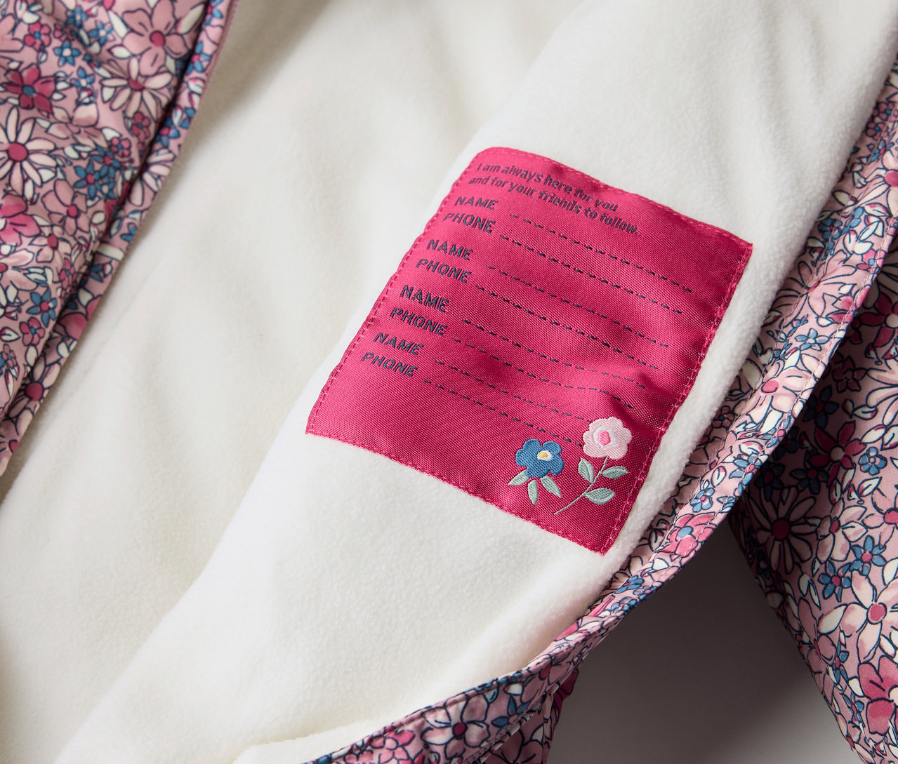 Detail zimního overalu pro miminka s květinovým vzorem a štítkem pro jméno.