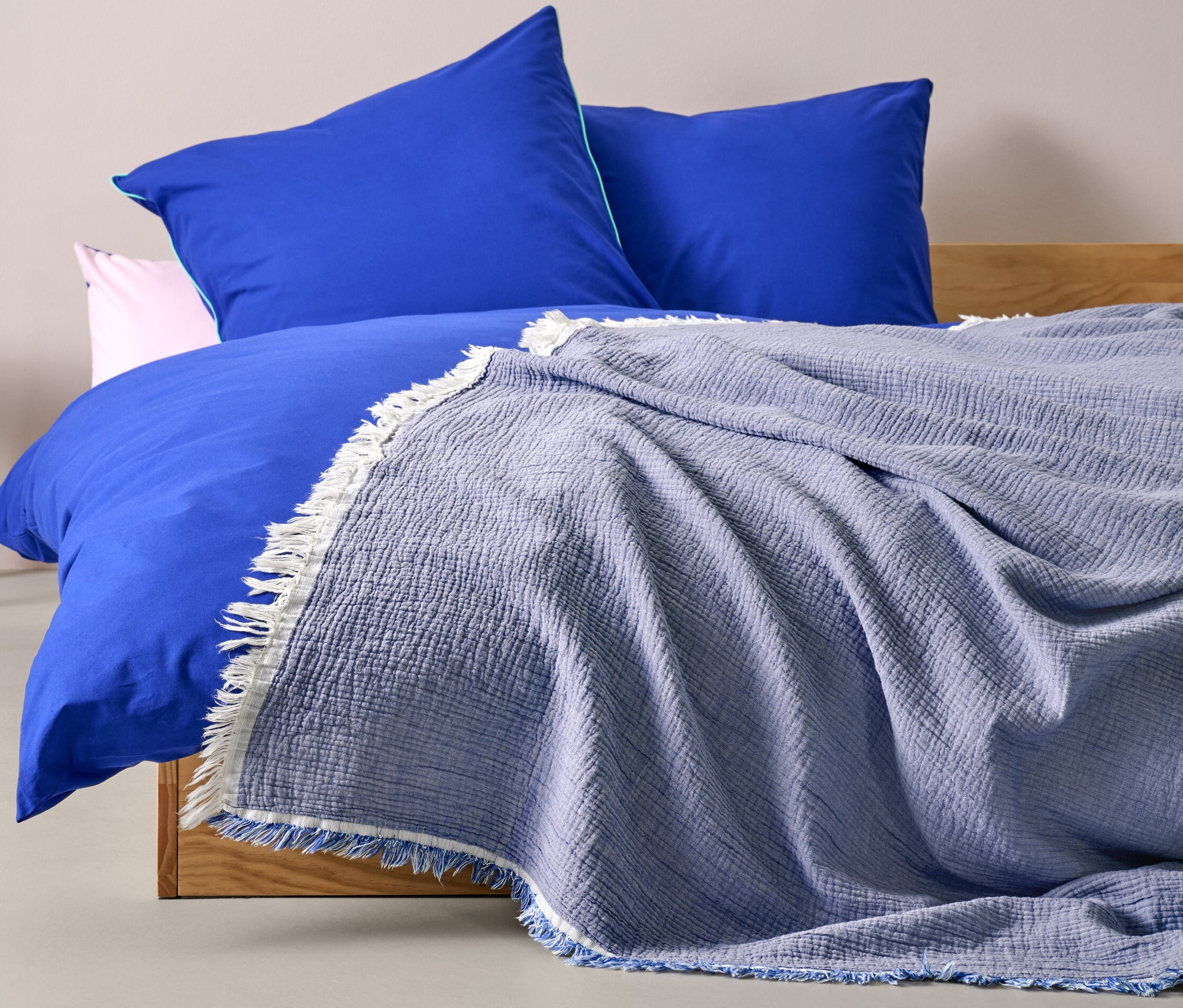 Na posteli leží modrý přehoz na postel o rozměrech 220 x 240 cm.