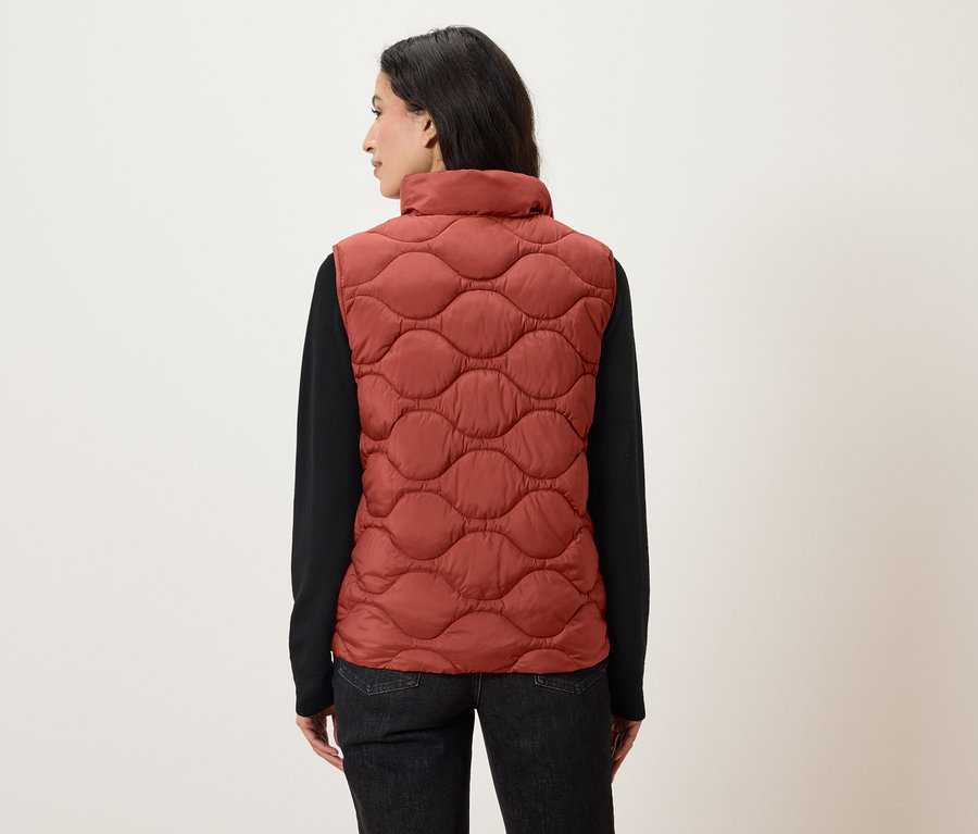 Žena zády k fotoaparátu má na sobě oranžovou prošívanou vestu a černou košili s dlouhým rukávem.