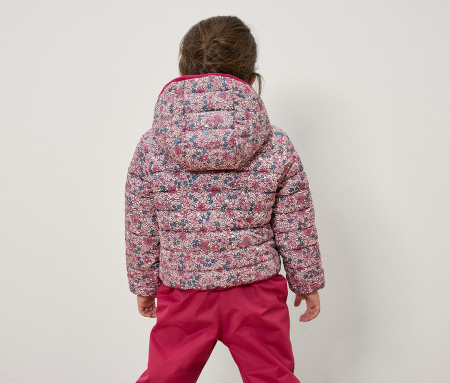 Dívka zády ke kameře má na sobě květinovou bundu a růžové kalhoty.