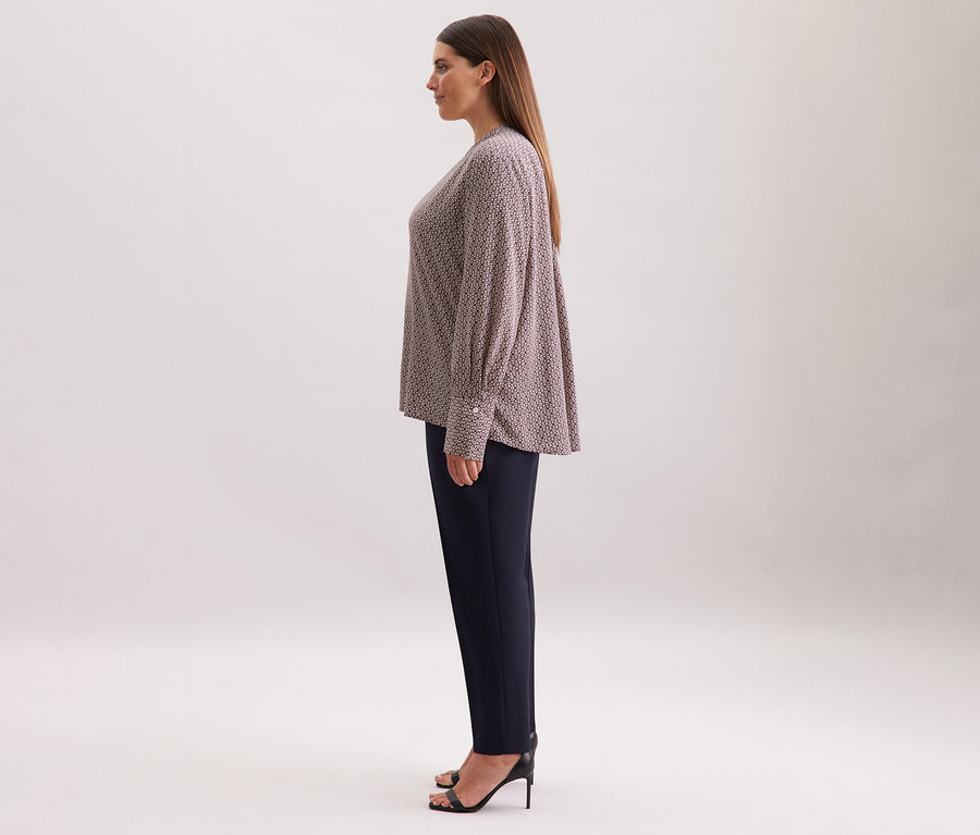 Žena má na sobě tuniku z viskózy Seidensticker s celoplošným potiskem v ecru a burgundské barvě, v kombinaci s tmavými kalhotami a černými botami na vysokém podpatku.