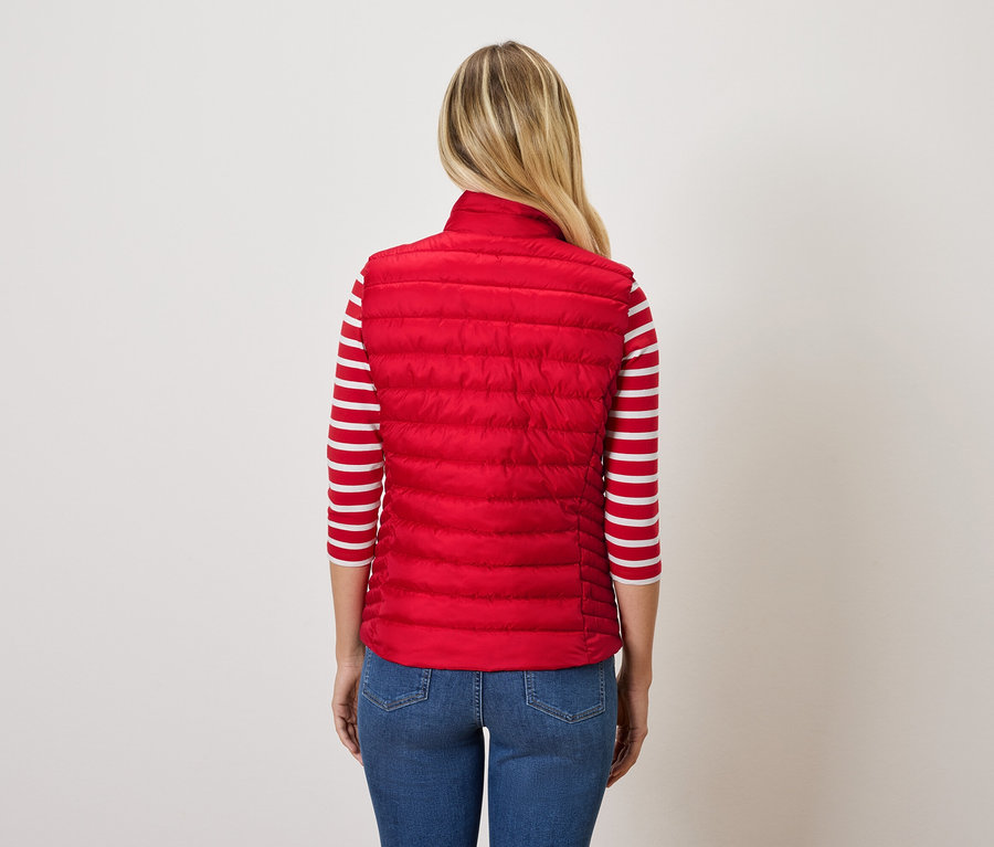 Zezadu je vidět žena s blond vlasy, oblečená do červené prošívané vesty a modrých džínů.