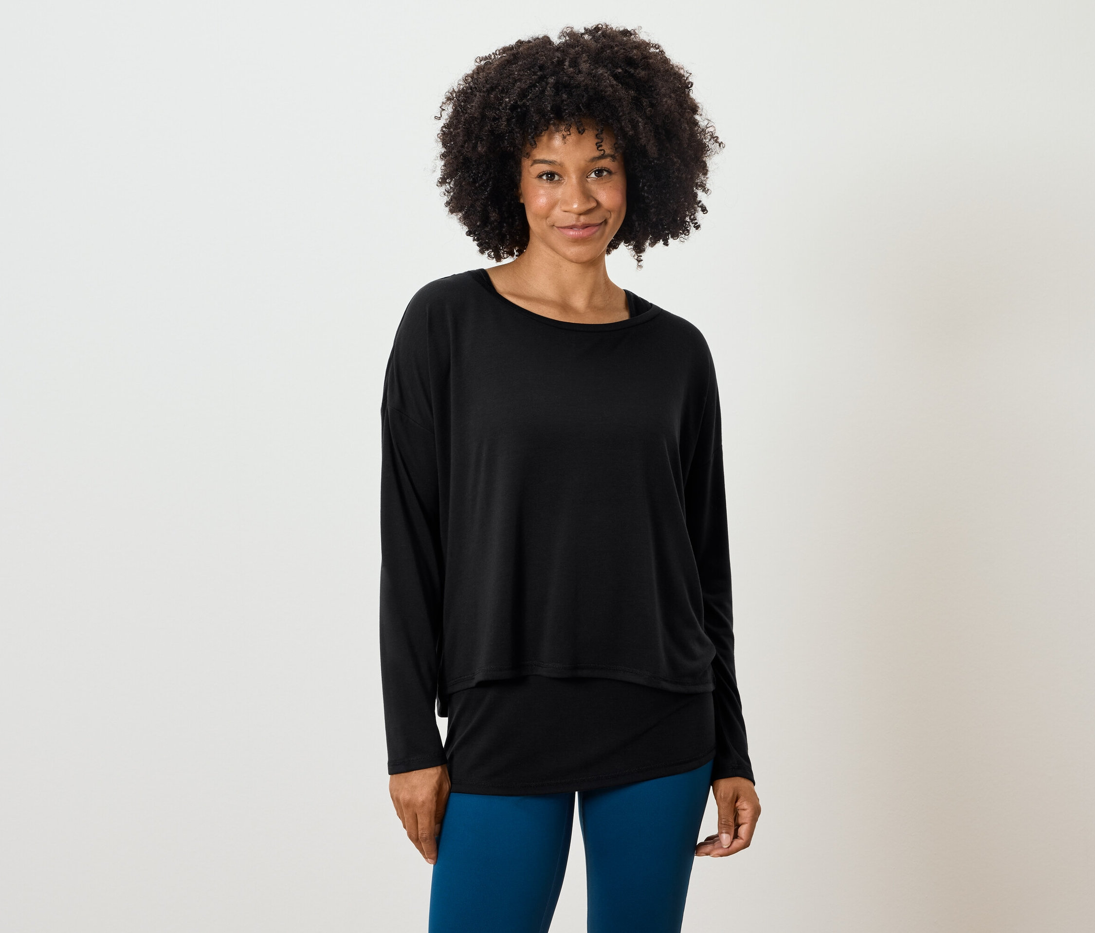 Žena s afro účesem pózuje v černém topu s dlouhým rukávem a modrých legínách.