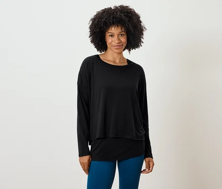 Žena s afro účesem pózuje v černém topu s dlouhým rukávem a modrých legínách.