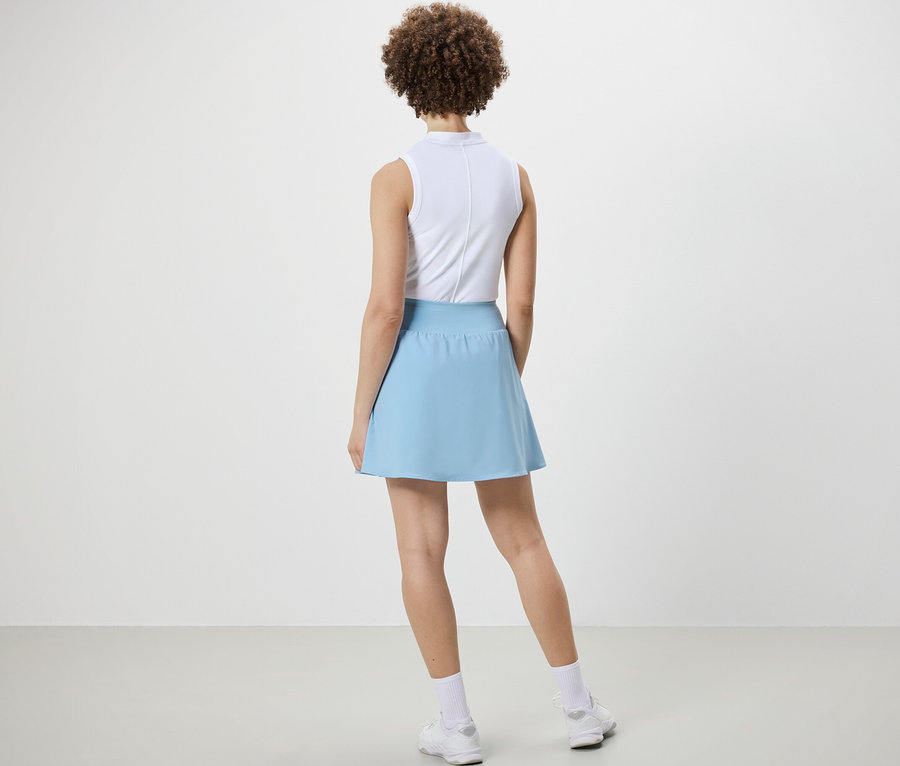 Žena stojí zády k fotoaparátu a má na sobě světle modrou sportovní sukni.