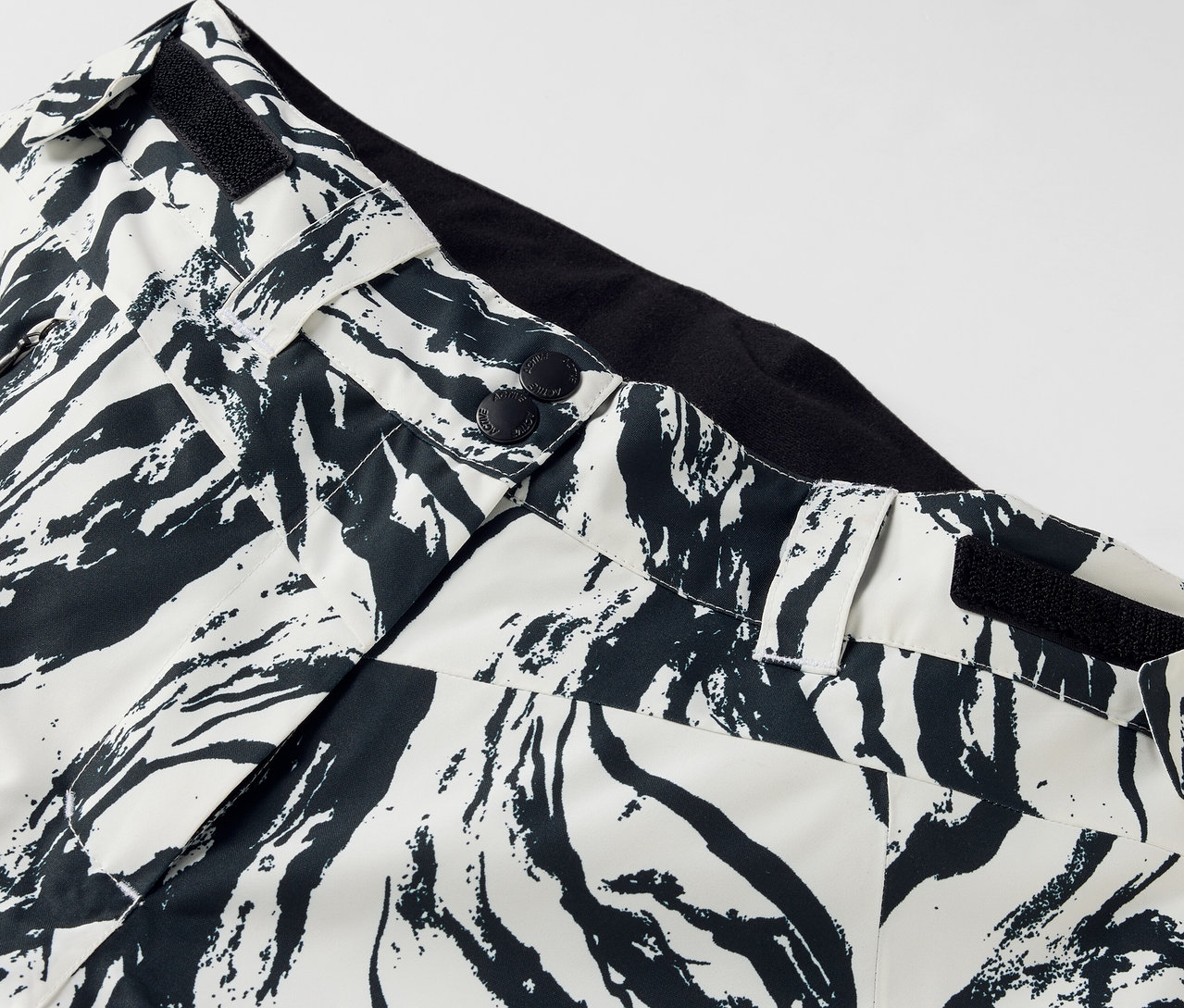 Detail kalhot s černobílým vzorem, zapínáním na knoflíky a černým pasem.