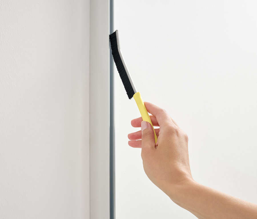 Ruka používá stěrku s žlutou rukojetí na skleněnou plochu.