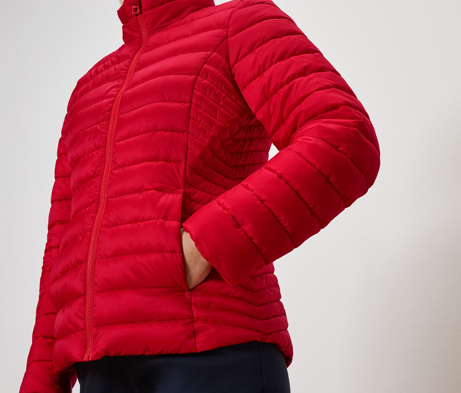 Osoba má ruku v kapse červené prošívané bundy.