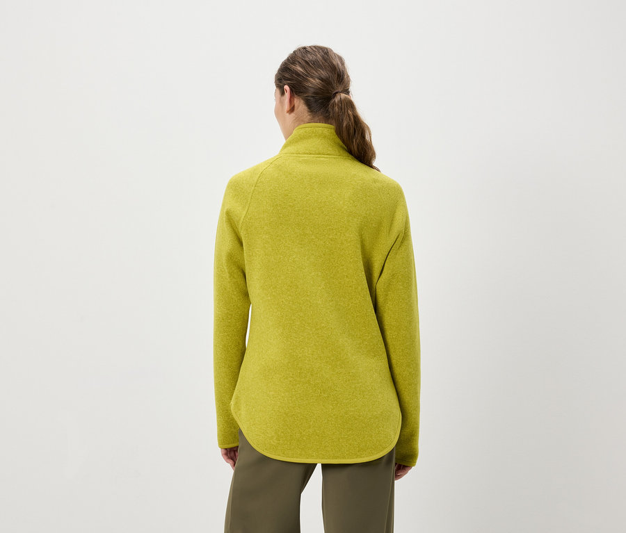 Zezadu pohled na ženu s vlasy staženými do culíku, která má na sobě žluto zelený fleecový pulovr a olivově zelené kalhoty.