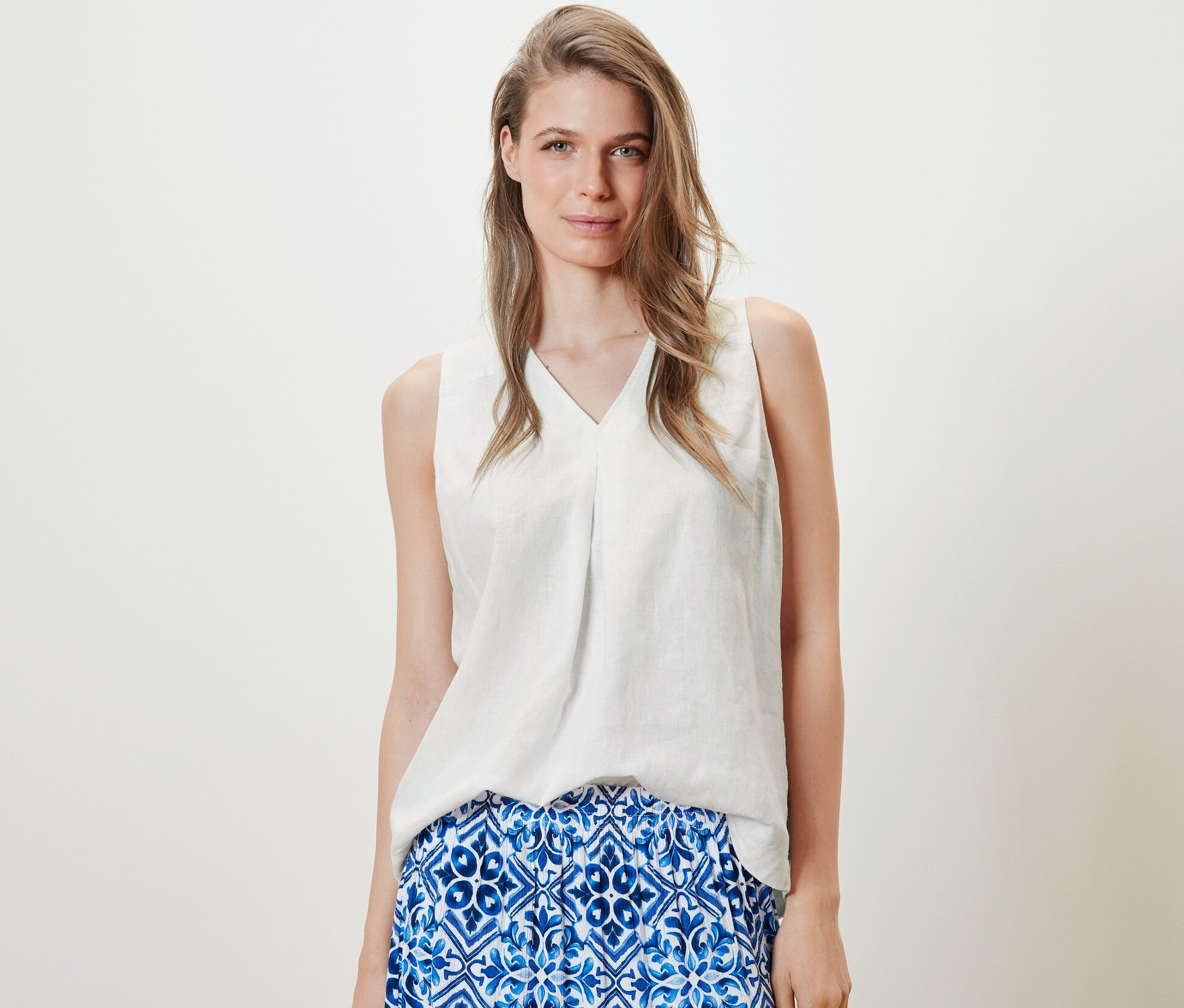 Žena má na sobě bílou lněnou halenku bez rukávů a modrou sukni.