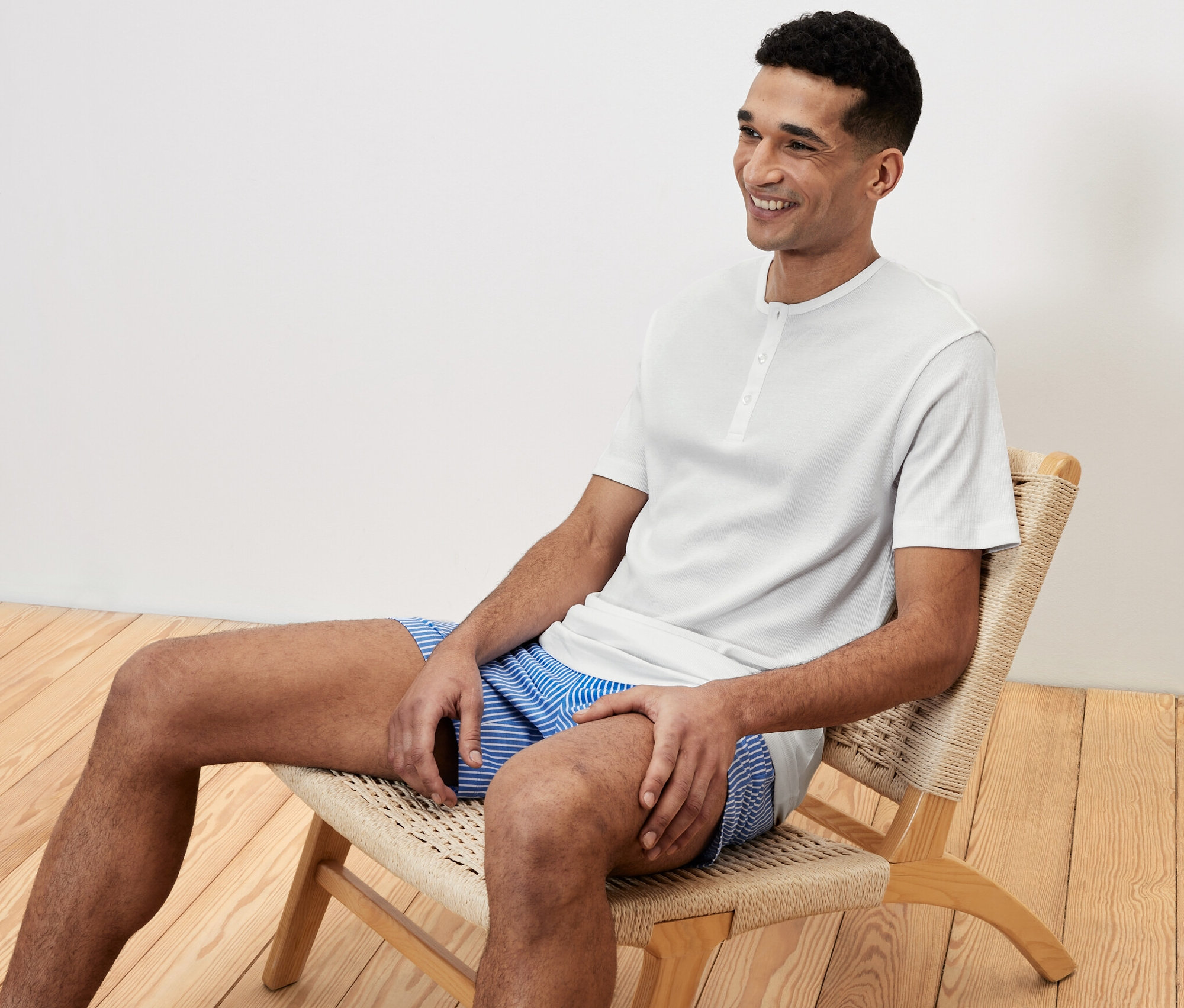 Muž sedí na židli v krátkém pyžamovém setu a usmívá se.