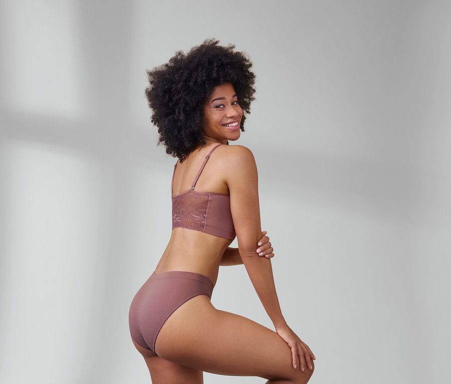 Žena pózuje v hnědé bezešvé podprsence s krajkou a hnědých bezešvých kalhotkách.