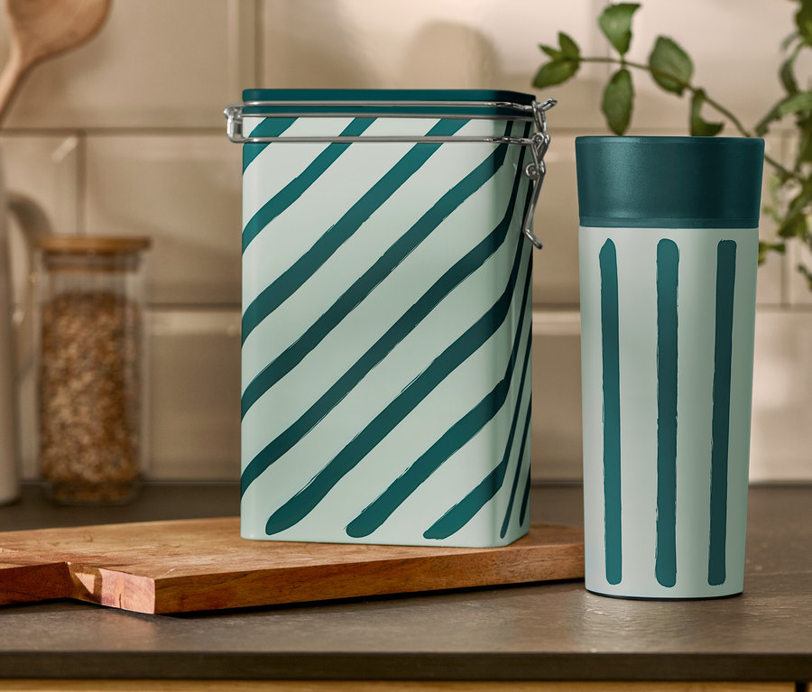 Na kuchyňském stole stojí pruhovaná dóza na kávu a šálek Coffee-to-go.