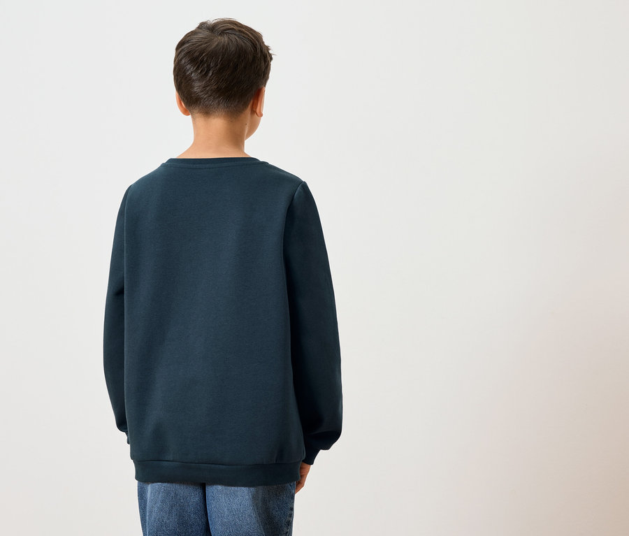 Pohled zezadu na dítě s tmavými vlasy v tmavě modré mikině a modrých džínách na bílém pozadí.