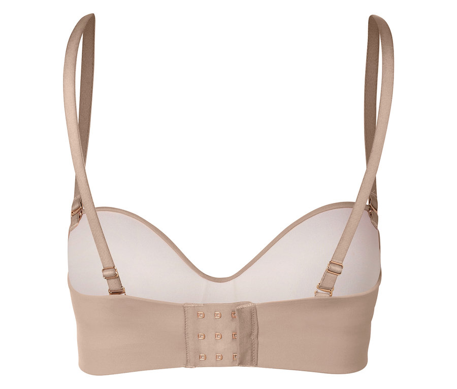 Detailní záběr na zadní část béžové podprsenky s nastavitelnými ramínky a háčkovým zapínáním.