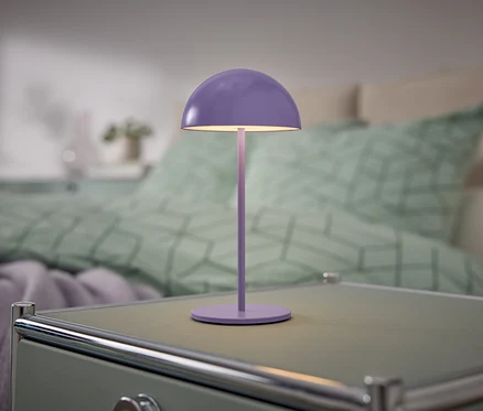 Fialová lampa stojí na nočním stolku vedle postele.