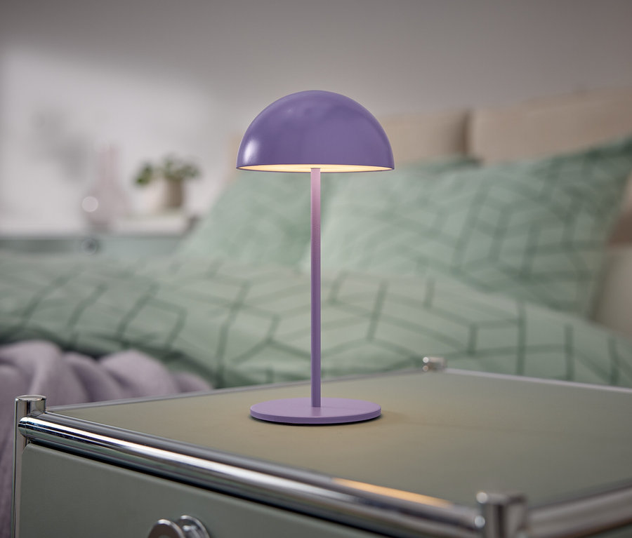 Fialová lampa stojí na nočním stolku vedle postele.