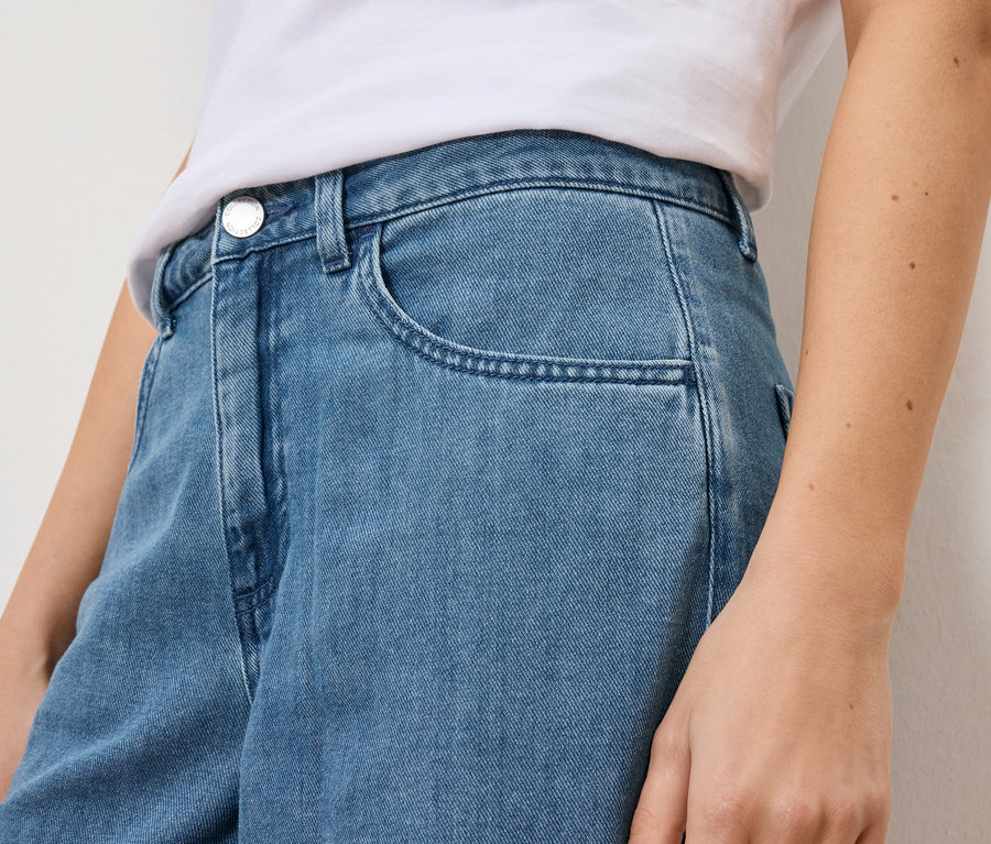 Detailní záběr ženy ve světle modrých džínách a bílém tričku.