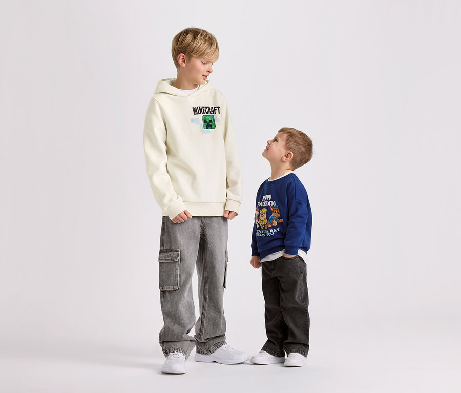 Dva chlapci stojí na bílém pozadí. Větší chlapec má na sobě dětskou mikinu s počesanou vnitřní stranou MINECRAFT.