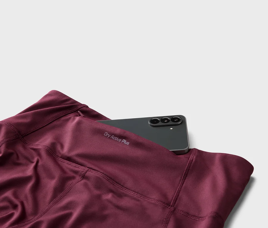 Detail bordových legín s nápisem „Dry Active Plus“ a černým smartphonem v kapse.