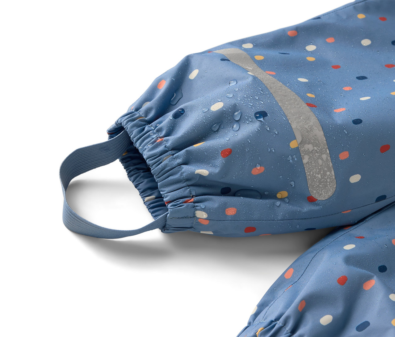 Detailní záběr na modrý overal do deště s barevnými puntíky a reflexním pruhem, na kterém jsou vidět kapky vody.