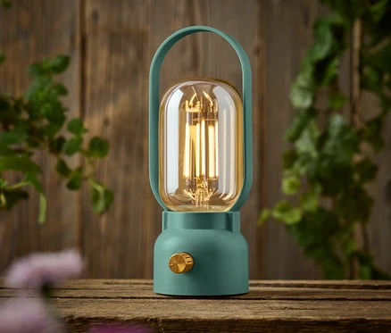 Zelená lampa se zlatým knoflíkem stojí na dřevěném stole.